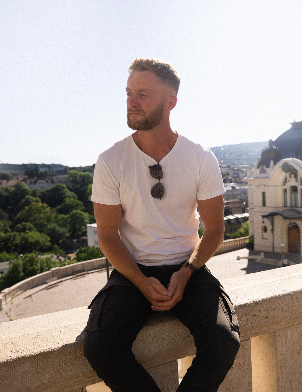Marcin sitzt auf einer Balustrade über der Stadt, Sonnenbrille im Kragen