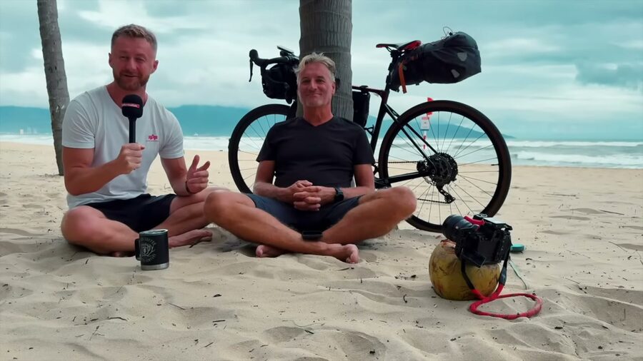 René und Marcin sitzen am Strand von Da Nang, dahinter Renés Reiserad